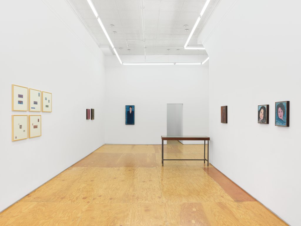 Installation view of Omara's exhibition at Margot Samel. Works on paper framed on the left wall, paintings hung sparsely and in pairs at times. Table with photographs.