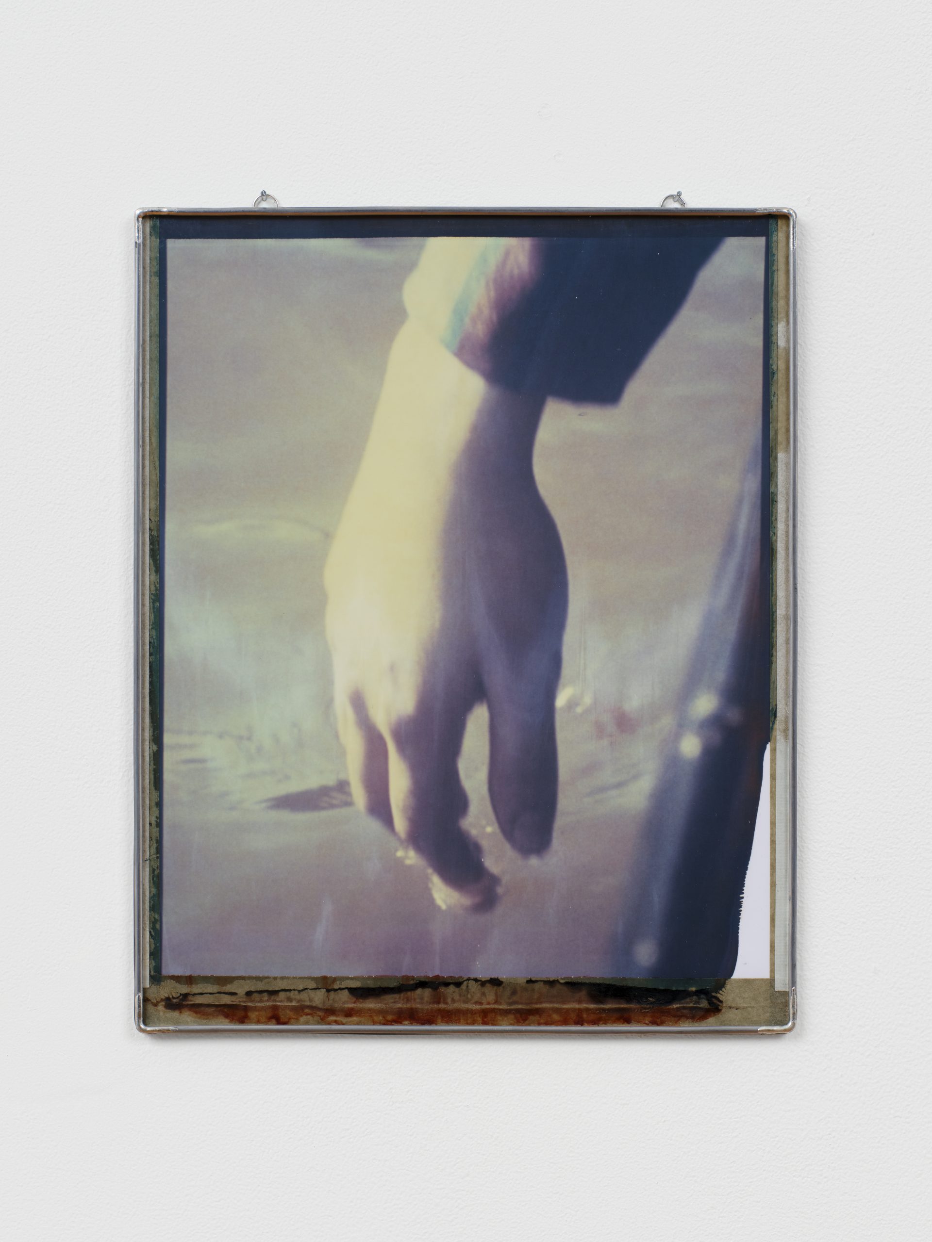 Photograph of a hand gently touching a body of water, framed in metal