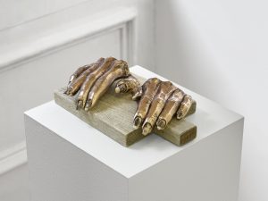 Sculpture of hands in Cast bronze with porcelain and ceramic decals (on-glaze) nails by Man Yau. Displayed on chopping board in a white pedestal.