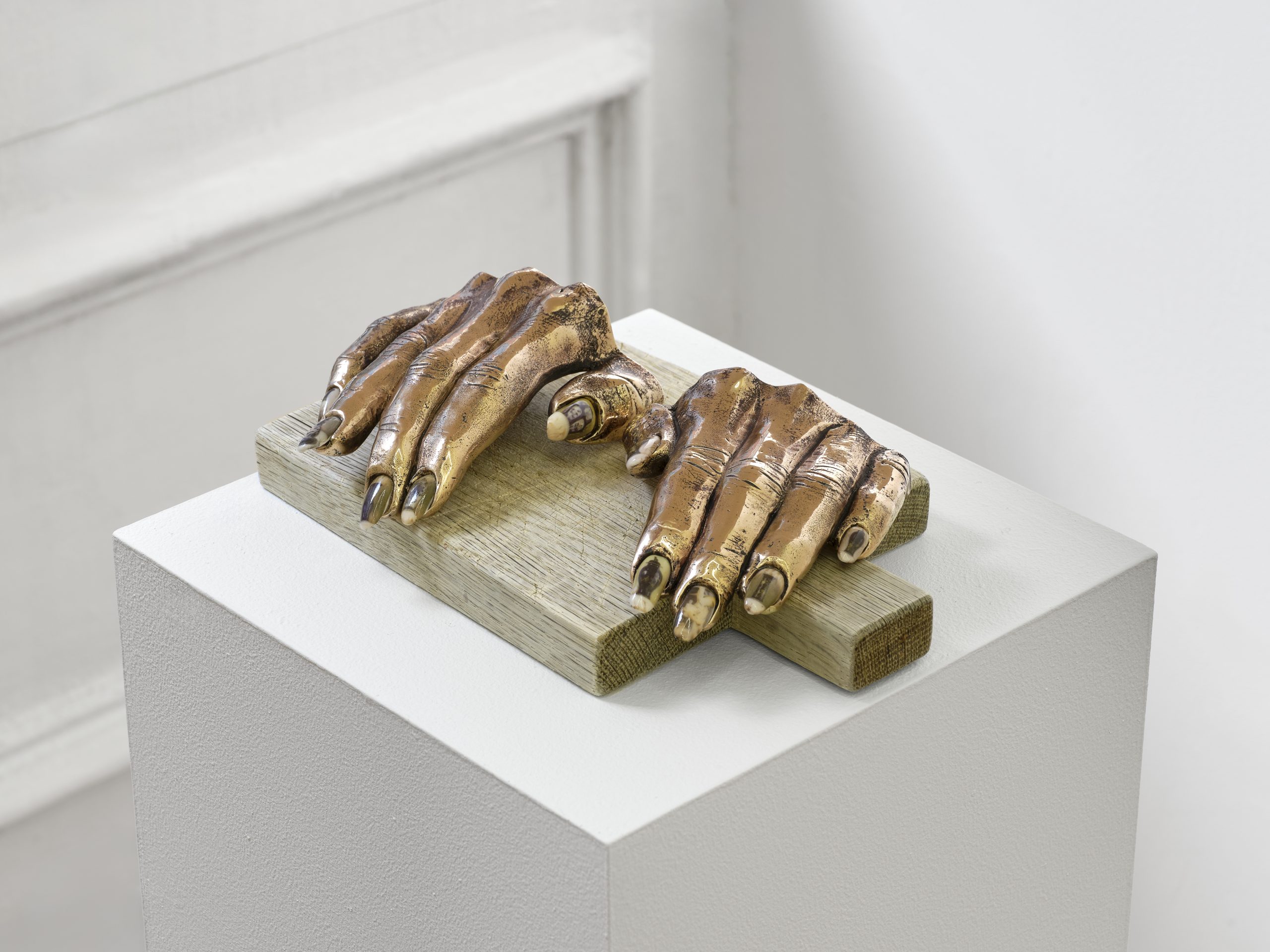 Sculpture of hands in Cast bronze with porcelain and ceramic decals (on-glaze) nails by Man Yau. Displayed on chopping board in a white pedestal.