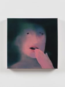 Blurred portrait of a pale face with a pink hand raised to an open mouth in a dark green haze.